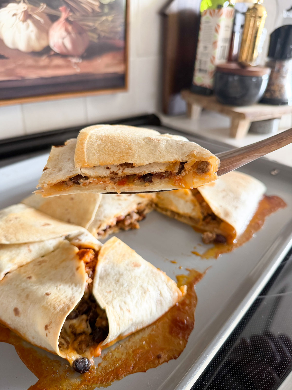 spatula holding up cut portion of sheet pan quesadilla. rest of quesadilla on sheet pan in the background.