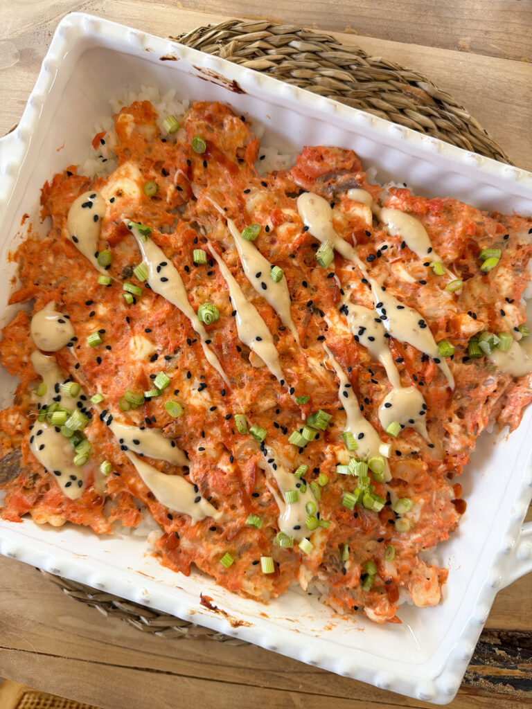 overhead shot of finished baked sushi bake in baking dish with drizzle of mayo, sesame seeds and scallions on top