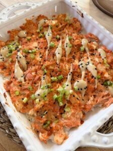 close up shot of finished baked sushi bake in baking dish with drizzle of mayo, sesame seeds and scallions on top