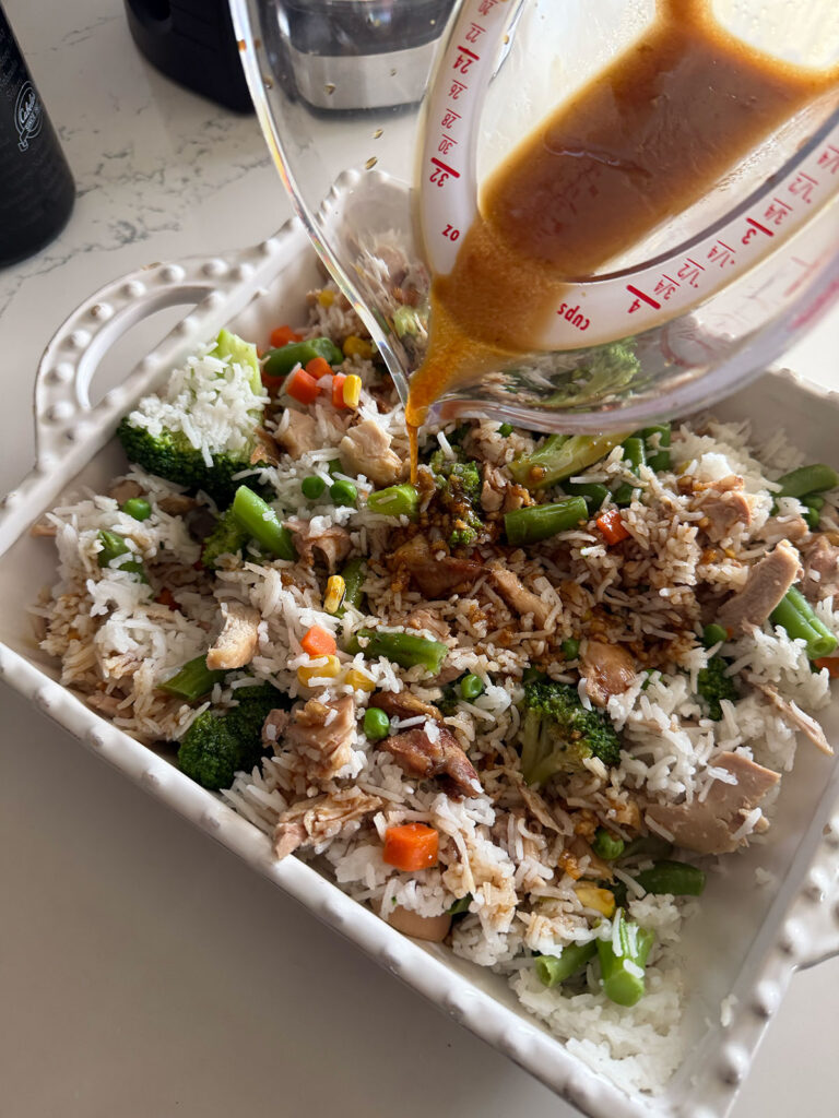 sauce being poured over unbaked chicken teriyaki casserole in white baking dish