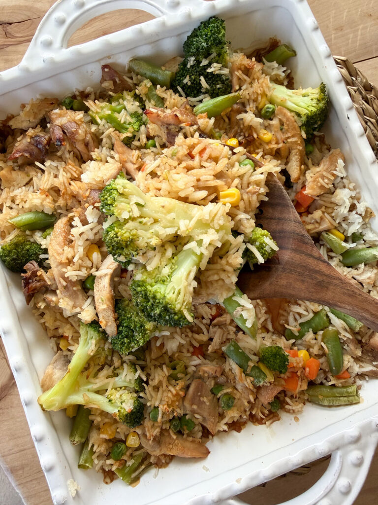 chicken teriyaki casserole in white baking dish with spoonful coming out on wooden spoon