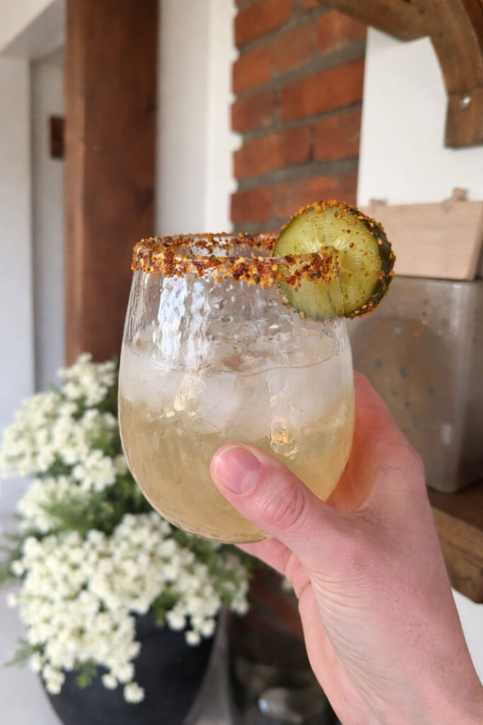 hand holding nice glass of pickle margarita with tajin rim and sliced pickle garnish