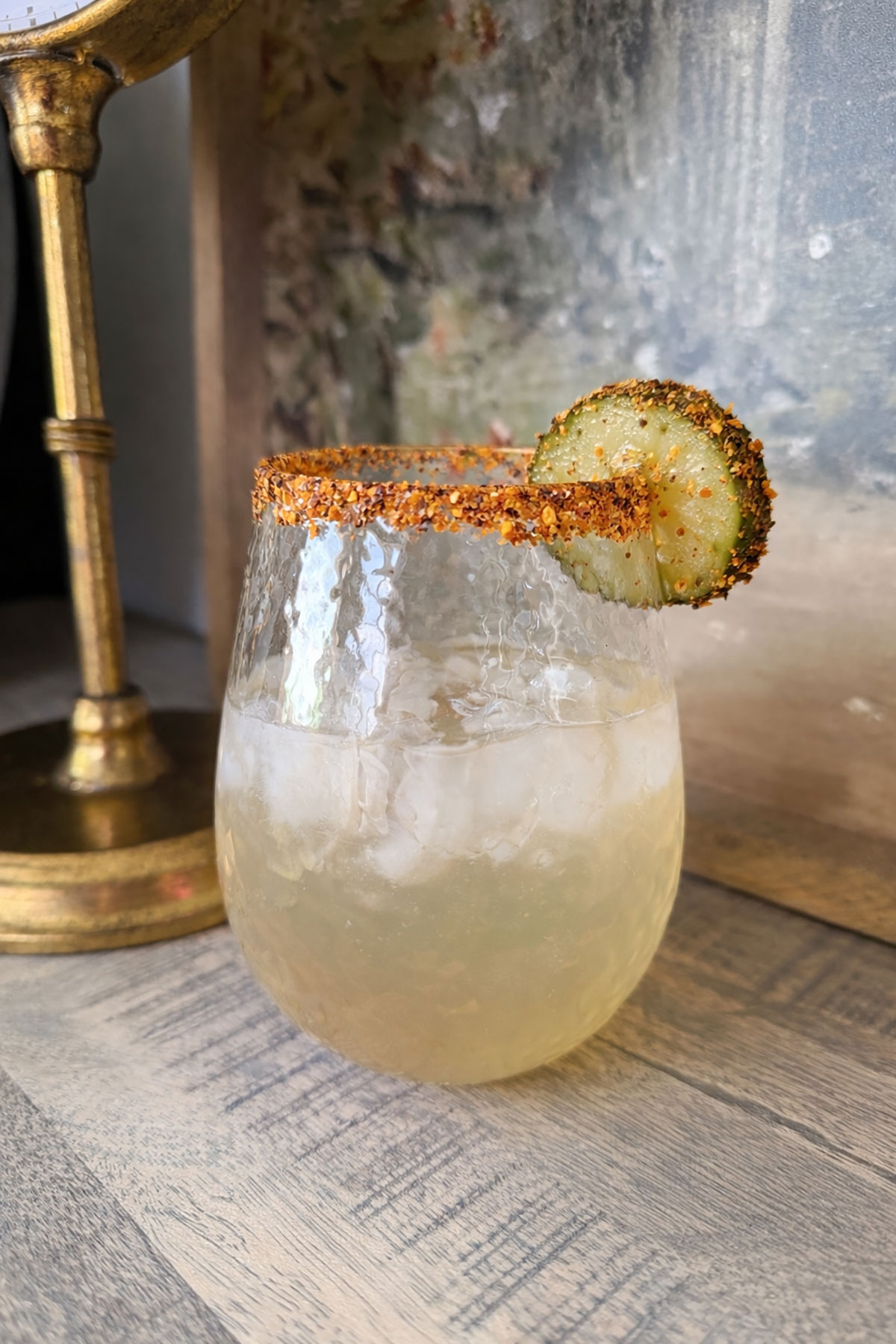 pretty glass of pickle margarita with tajin rim and pickle slice garnish on table top