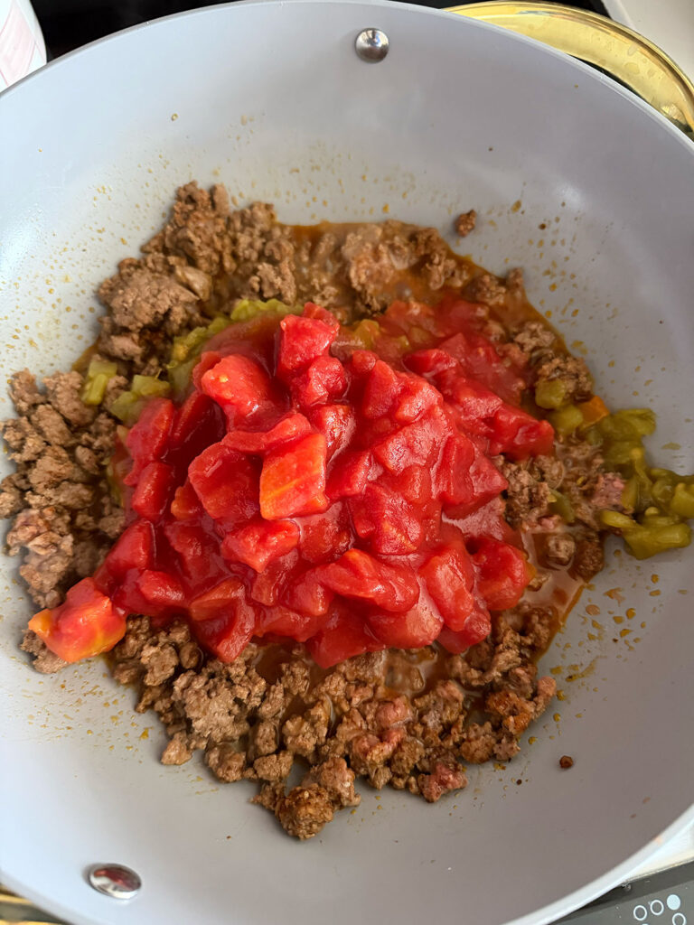 taco meat, canned chilis and canned tomatoes in pan
