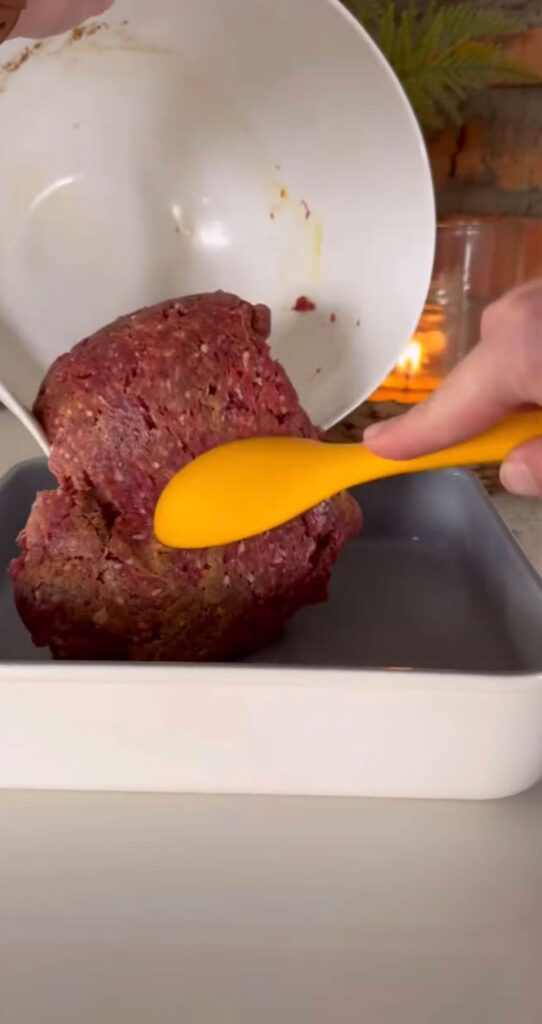 seasoned meat mixture being added to pan from bowl with orange spatula