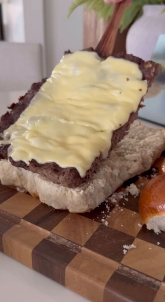 sheet pan burger patty topped with cheese being added to bottom layer of buns