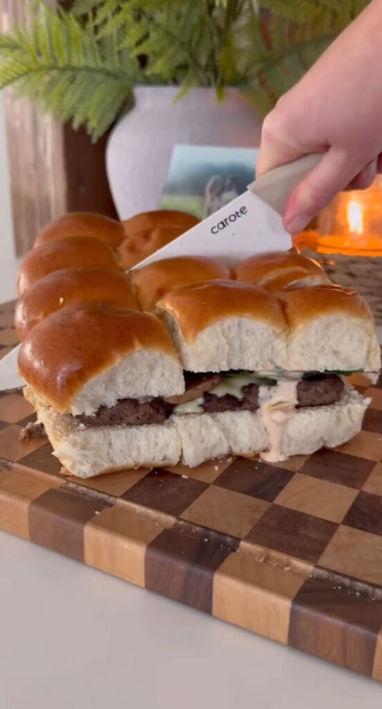 knife cutting into sheet pan burgers on checkered cutting board