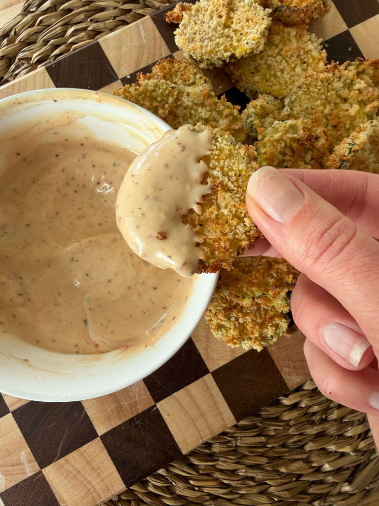 A hand holding an air fryer dill pickle that's dipped in sauce.