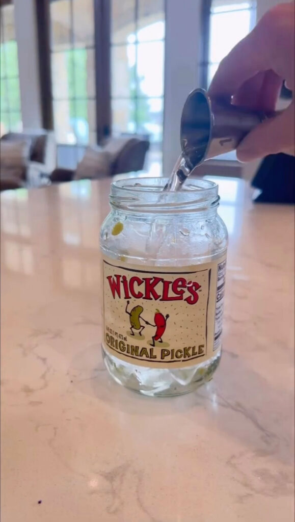 tequila being measured and added into pickle jar