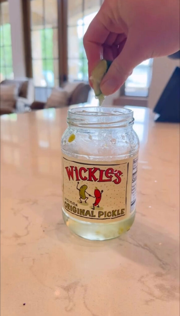 lime wedge being juiced into pickle jar