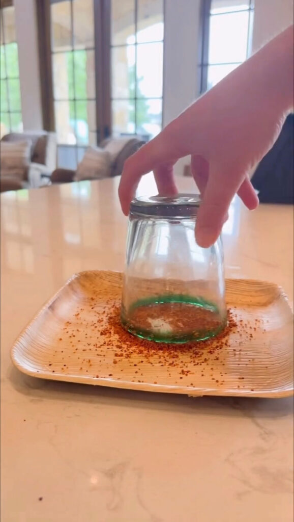 hand holding glass upside down in tajin on tray to dip the rim in