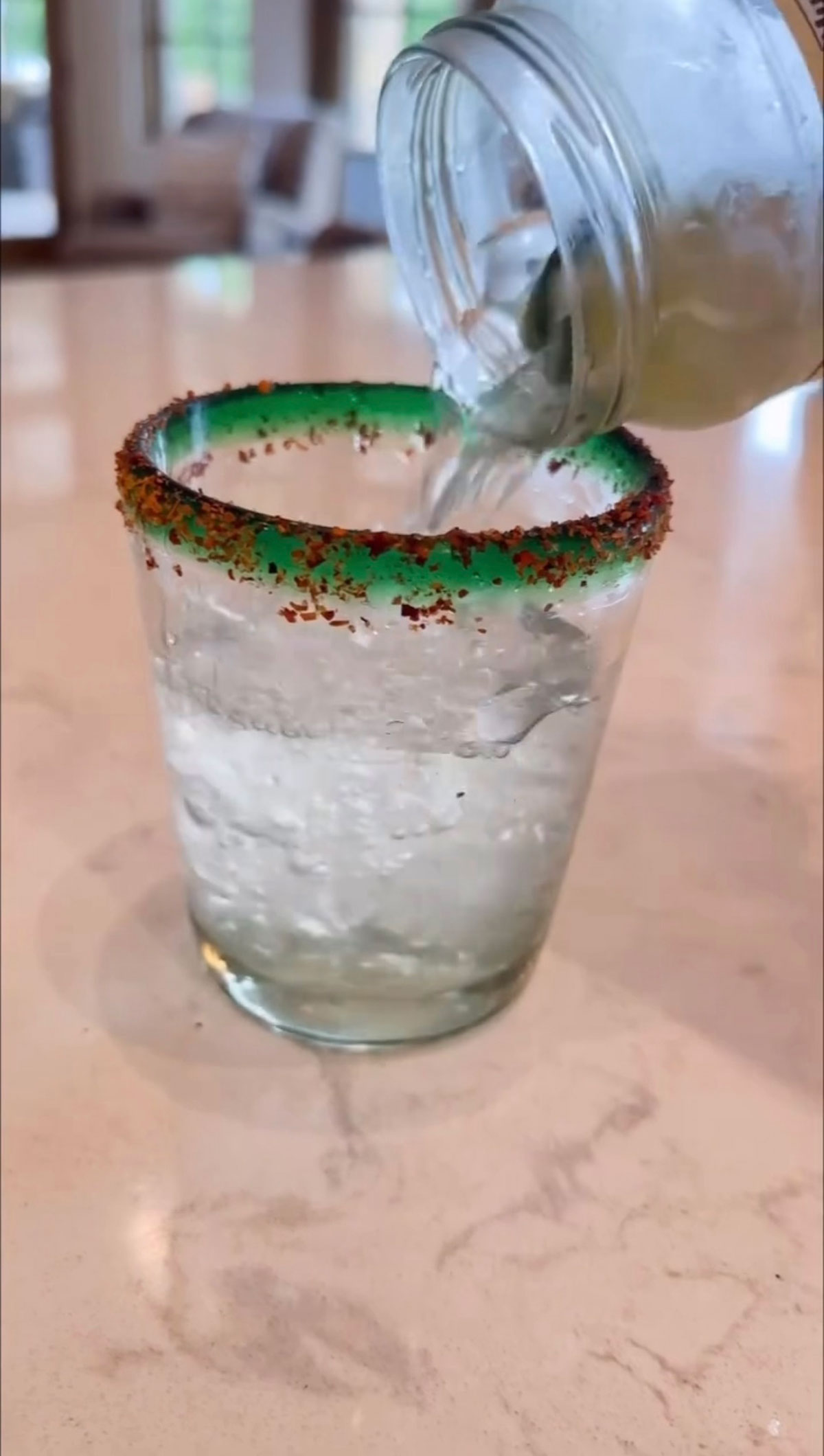 pickle margarita being poured into tajin rimmed glass