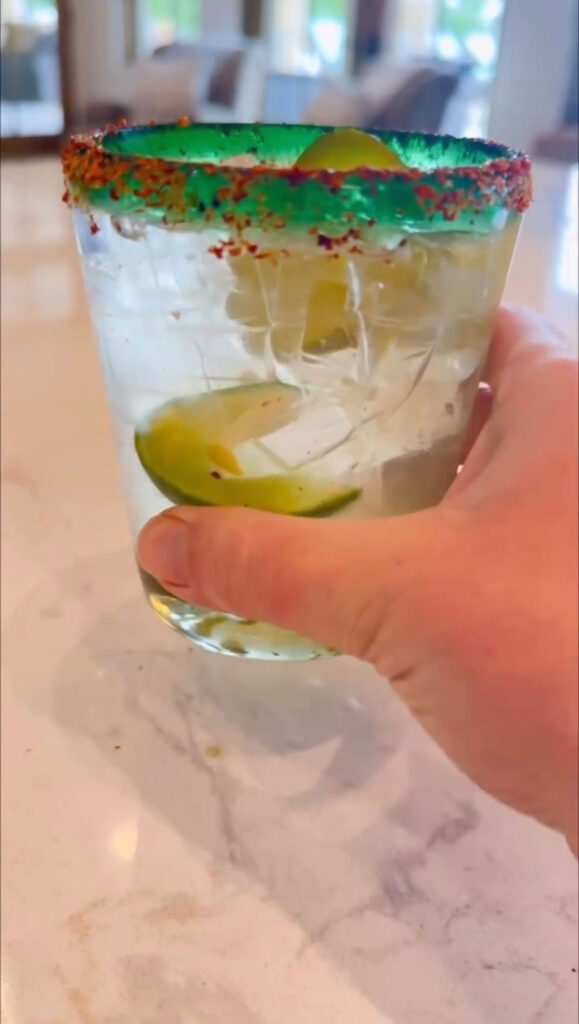 hand holding pickle margarita with tajin rim over counter