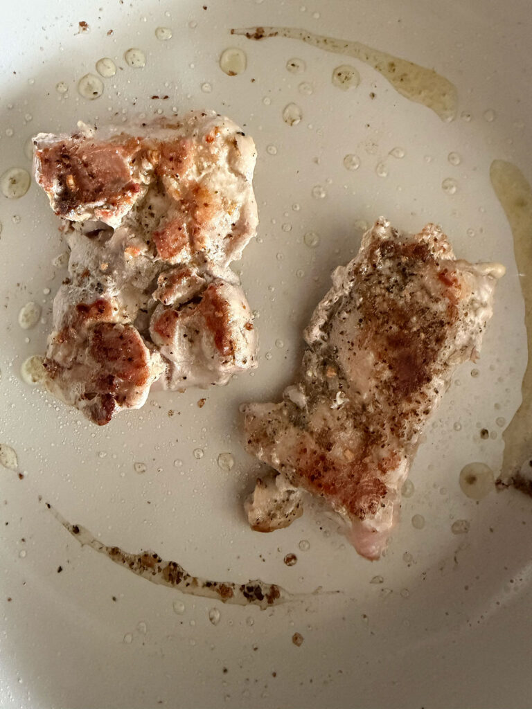 Searing chicken thighs in a white skillet. 