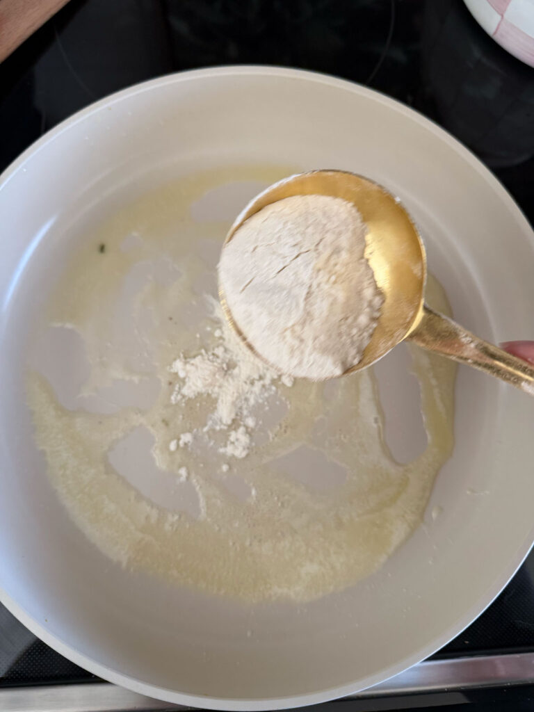 flour in gold measuring cup going into pot with melted butter