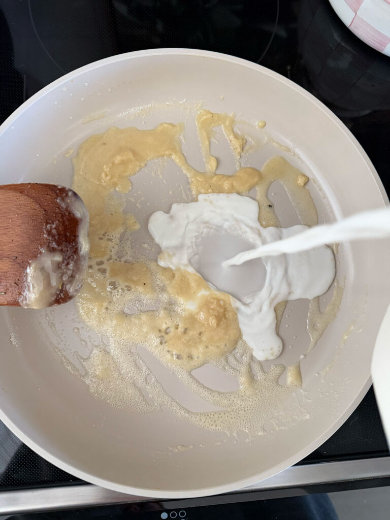 milk being poured into flour butter mixture in pot with wooden spoon
