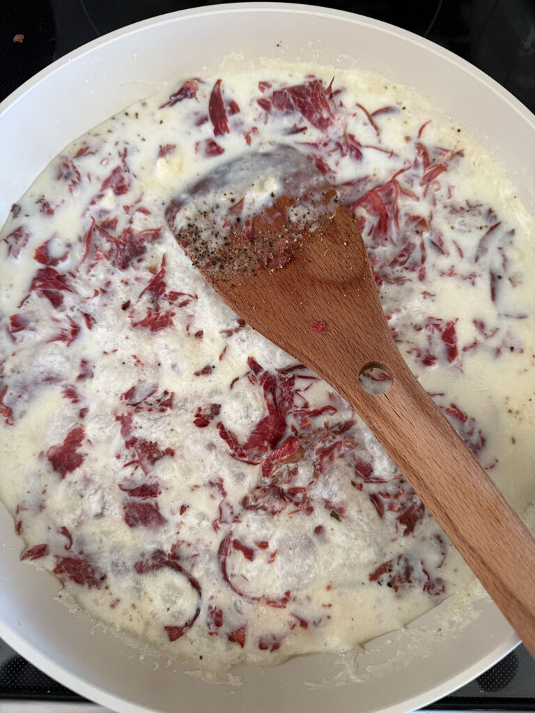 beef stirred into creamy sauce in pot with wooden spoon