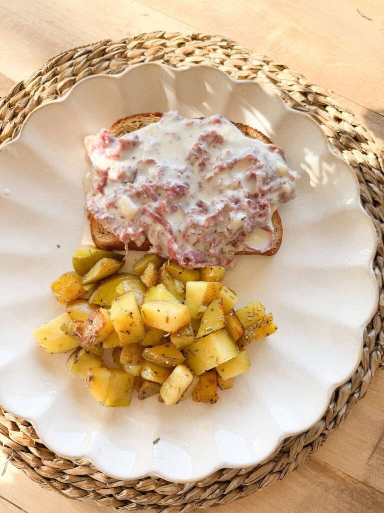 overhead view of cream chipped beef on toast next to home fry potatoes on white scalloped edge plate
