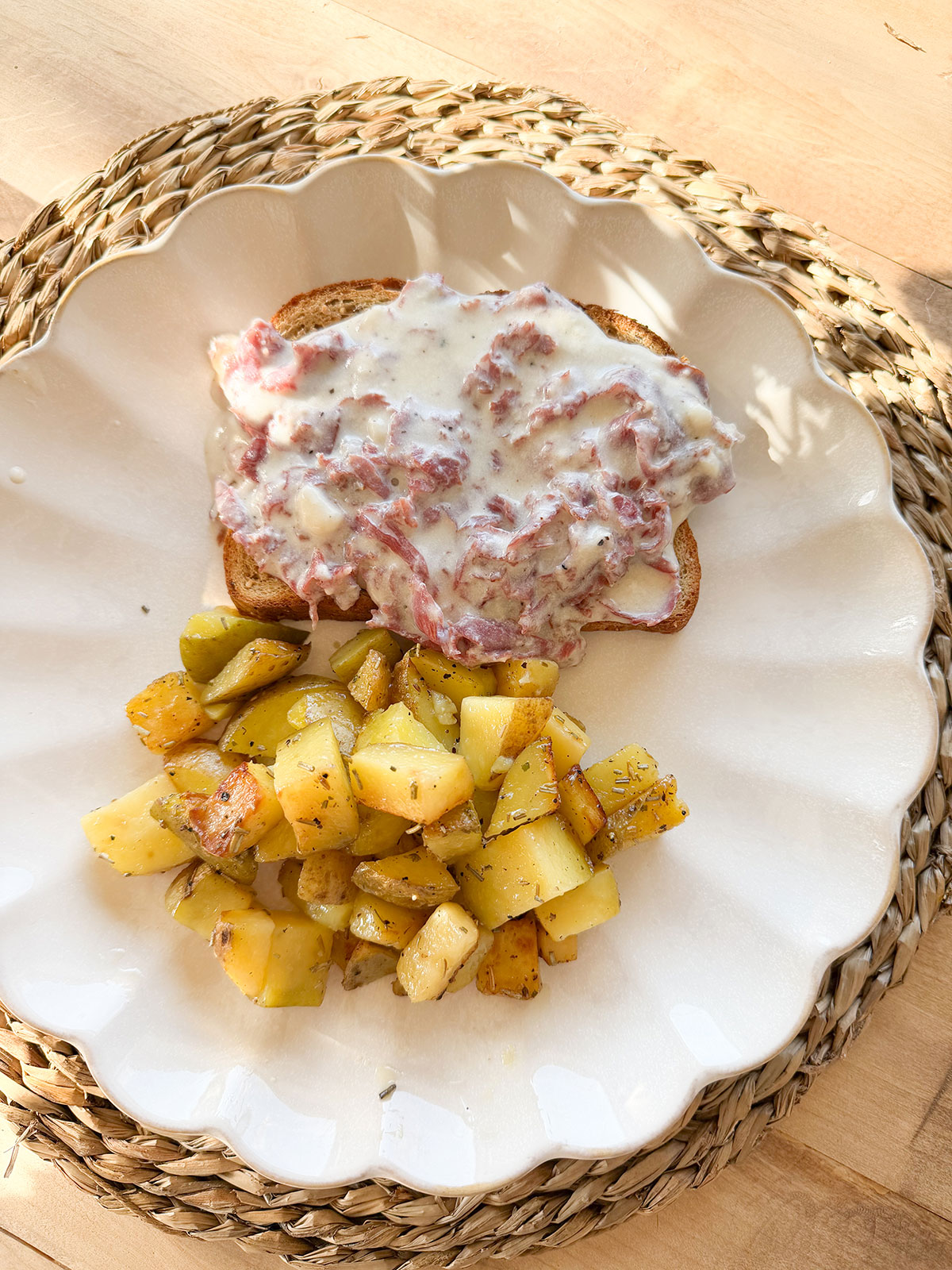 birds eye view of cream chipped beef on toast next to home fry potatoes on white scalloped edge plate