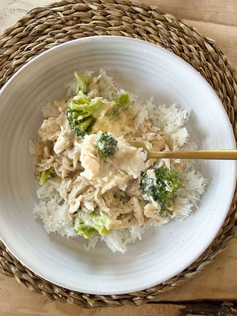 chicken divan over rice on white plate with gold forkful of chicken and broccoli