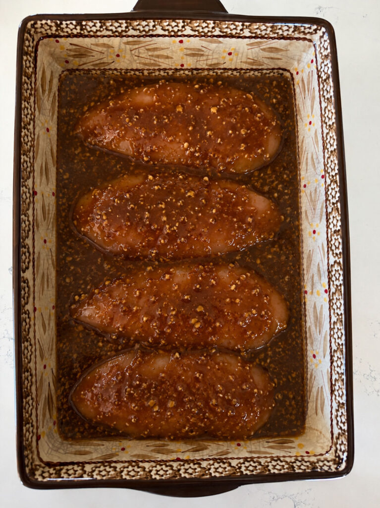 raw chicken breasts covered with sauce in casserole dish