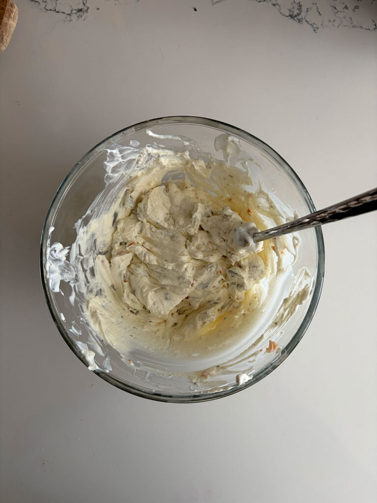 olive dip mixed in clear bowl on counter with spoon in it
