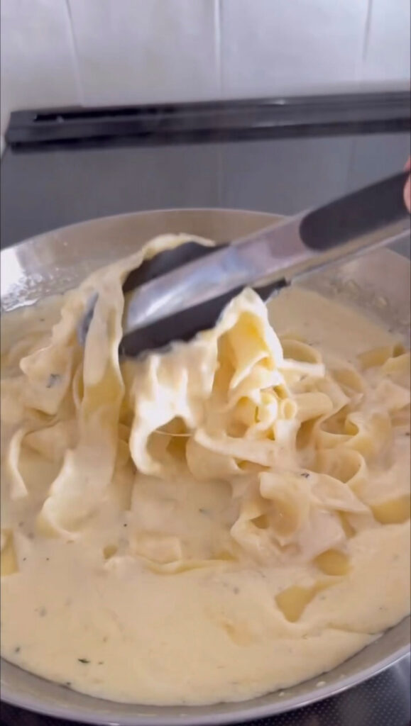 pasta and alfredo sauce in pan with tongs