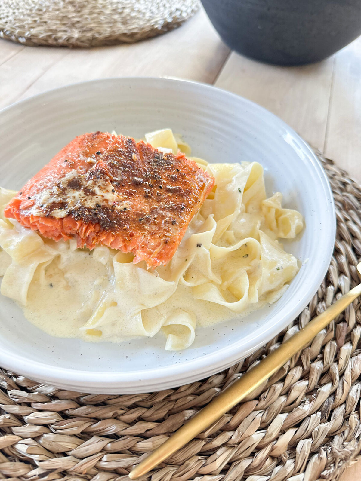 Finished plate of salmon alfredo in white bowl on placemat