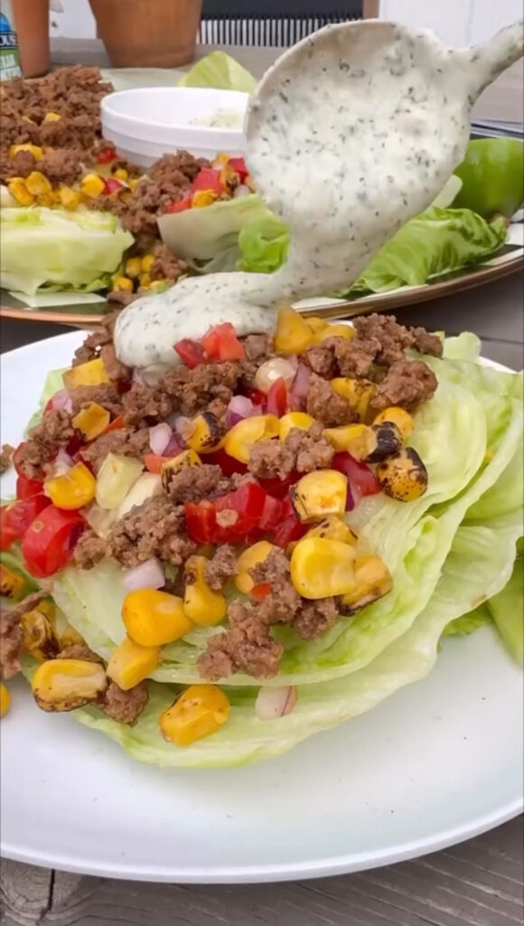 white plate with serving of taco salad on it with spoon adding dressing. platter of taco salad in background.