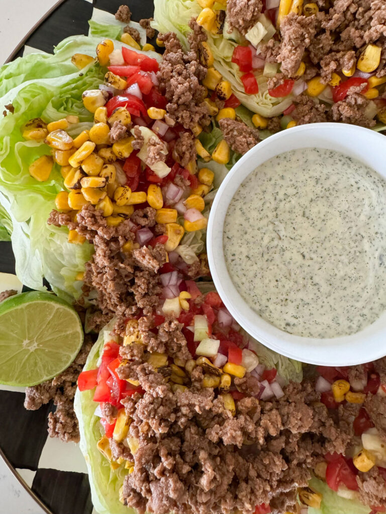 Finished taco salad on plate with dressing in the middle in a white bowl with a lime garnish