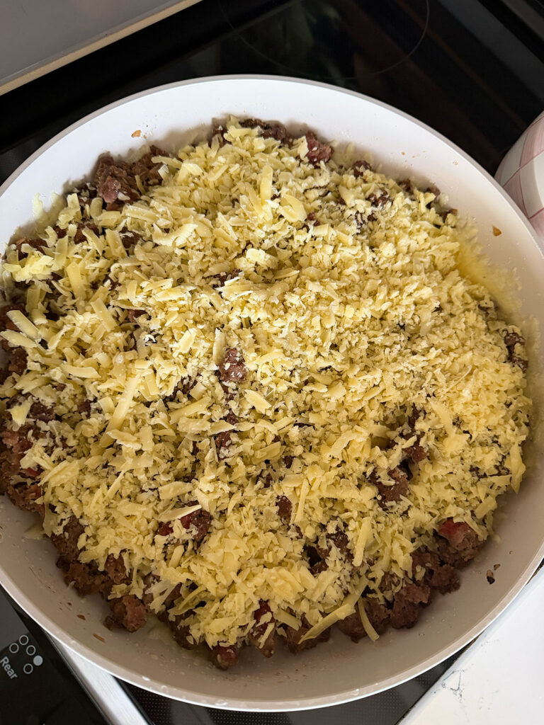 browned ground beef in pan topped with shredded cheddar cheese