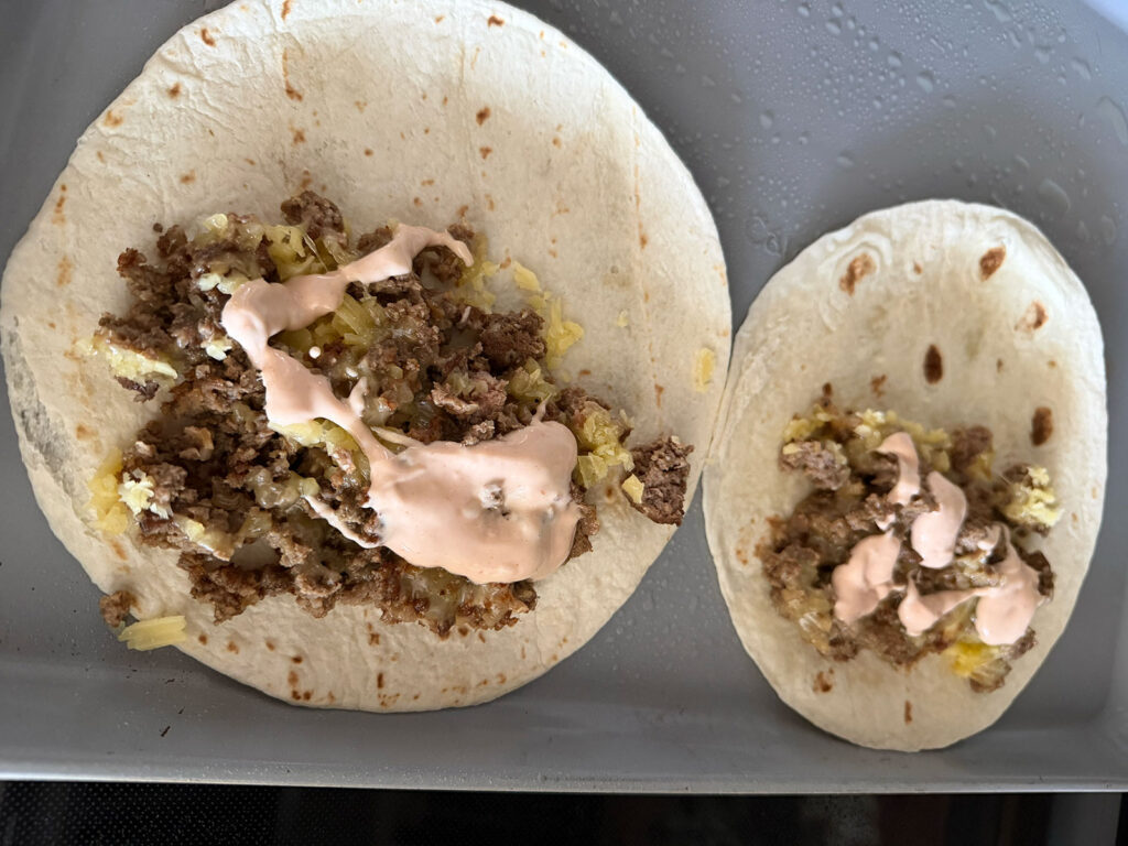 two cheeseburger tacos open faced on pan topped with ground beef mixture, cheese, and fry sauce, ready to be bal