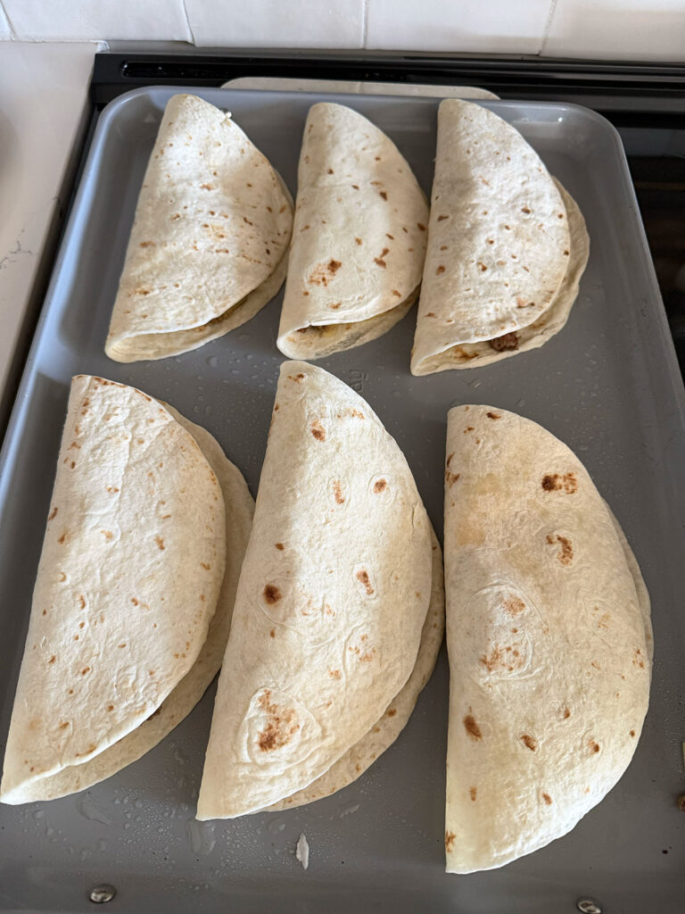 six cheeseburger tacos on pan ready to be baked