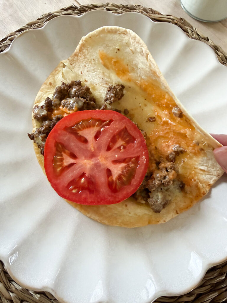 cheeseburger taco on white plate opened to show sliced tomato