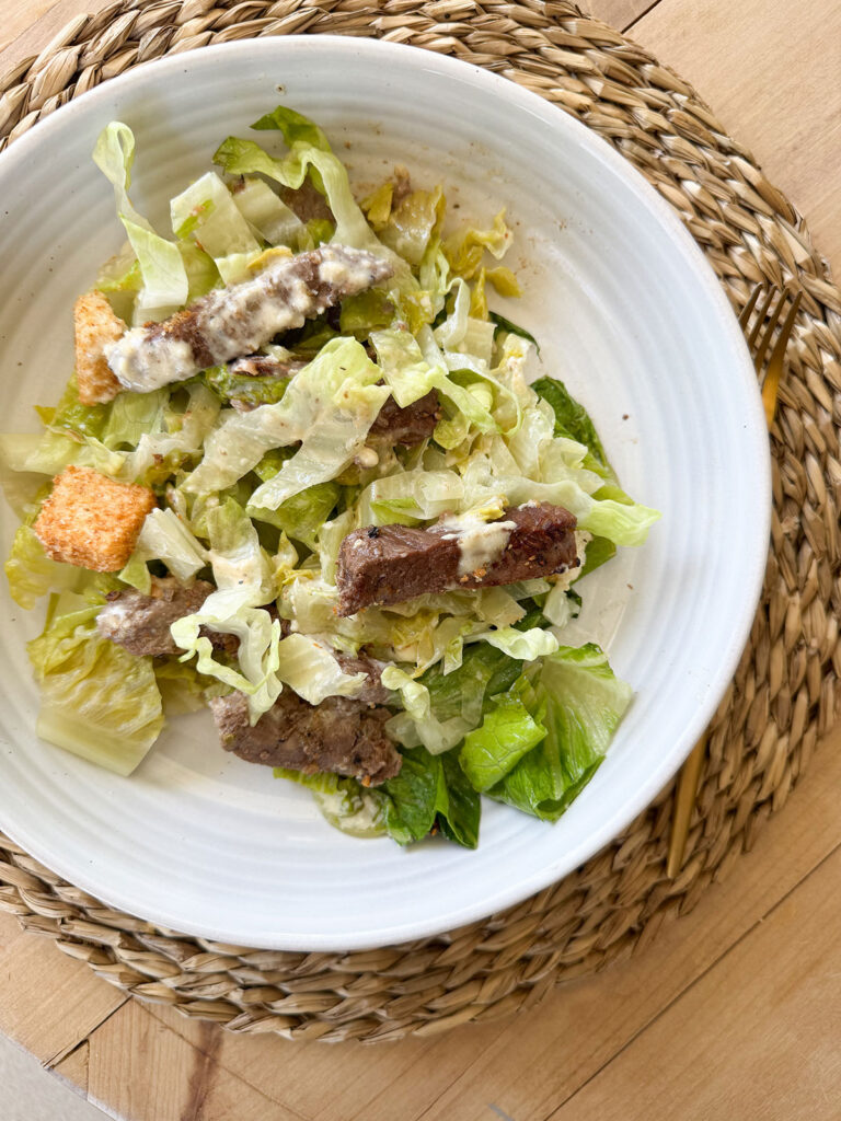 steak caesar salad on white plate on placemat