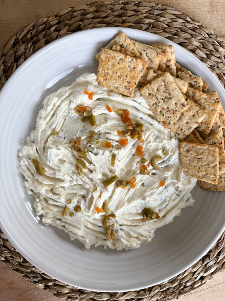 olive dip in white bowl with crackers in a pile on the side