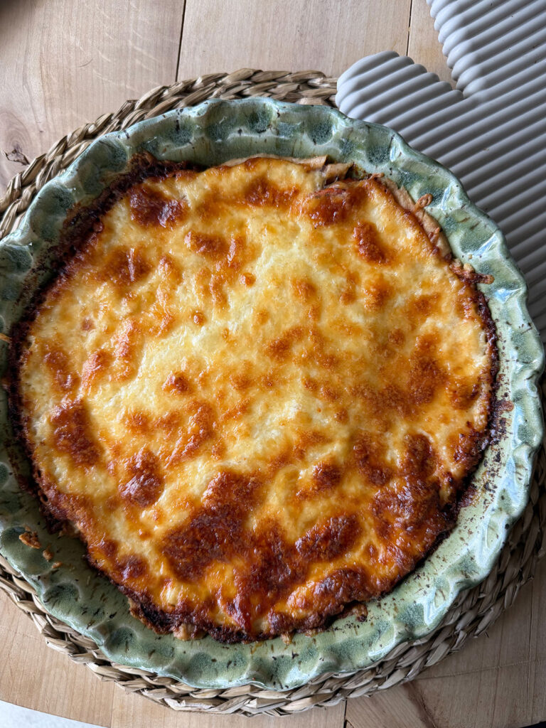 finished baked tomato pie in green pie dish on placemat with oven mitt next to it