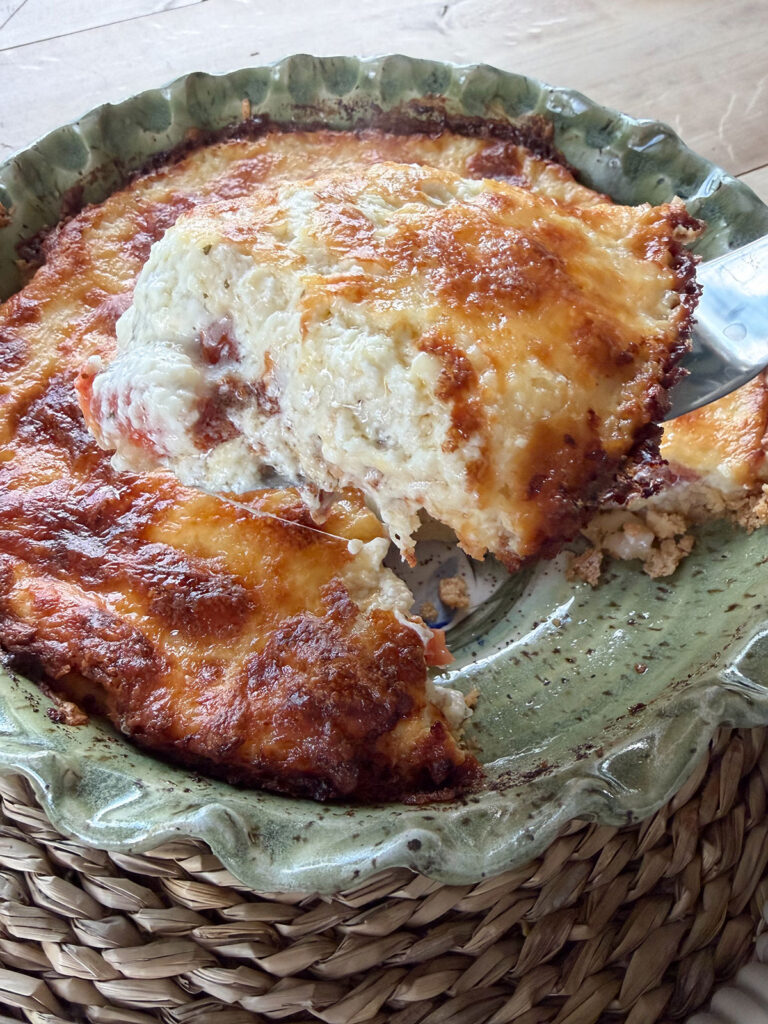 baked tomato pie in green dish with spatula removing a slice