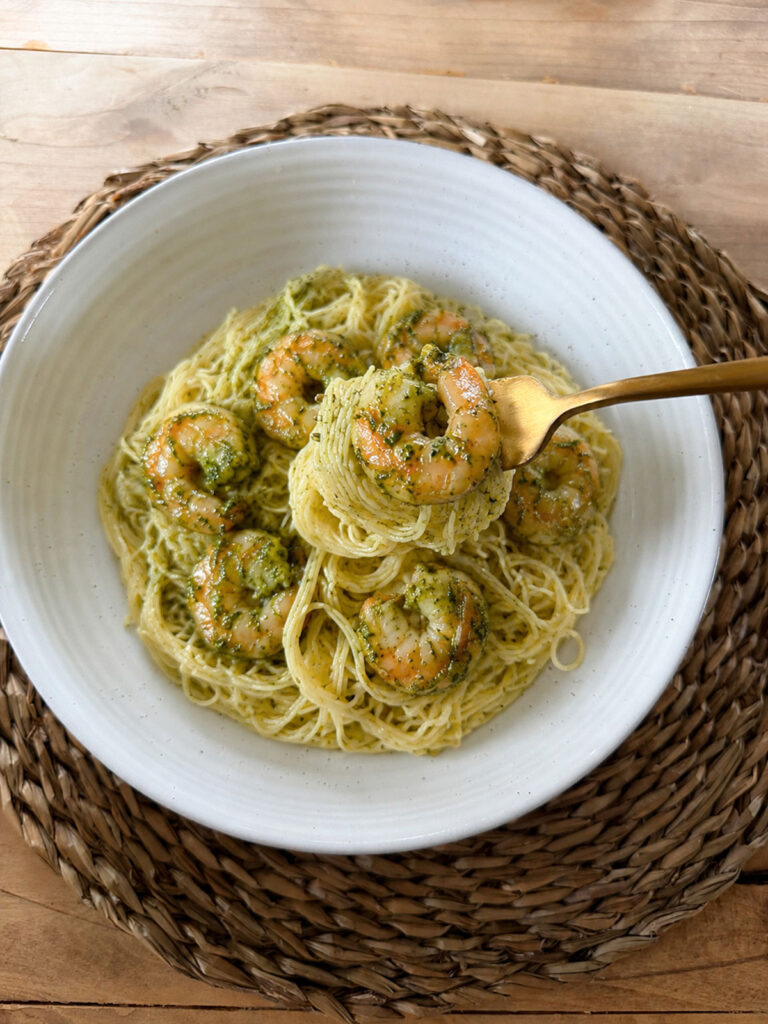 finished white plate of shrimp pesto pasta with a gold forkful of pasta on it