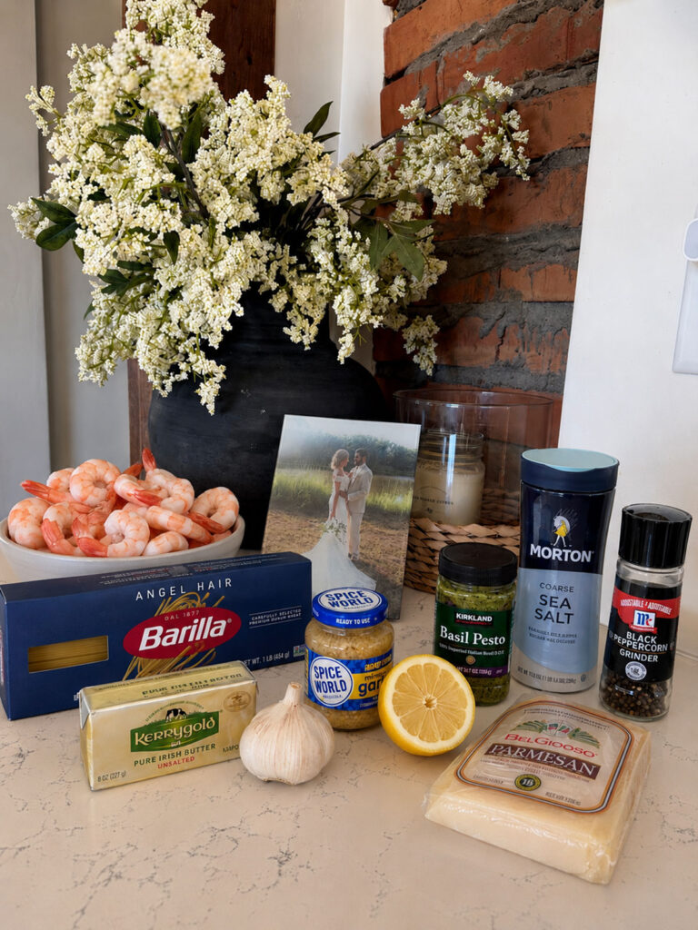 shrimp pesto pasta ingredients on counter with flowers in background.