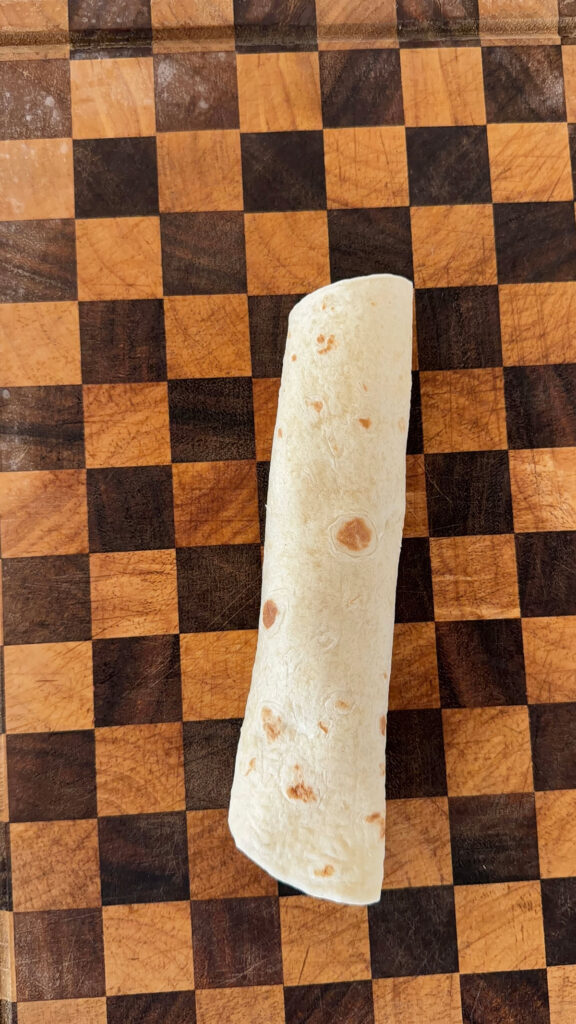 A checkered cutting board with a tortilla rolled.