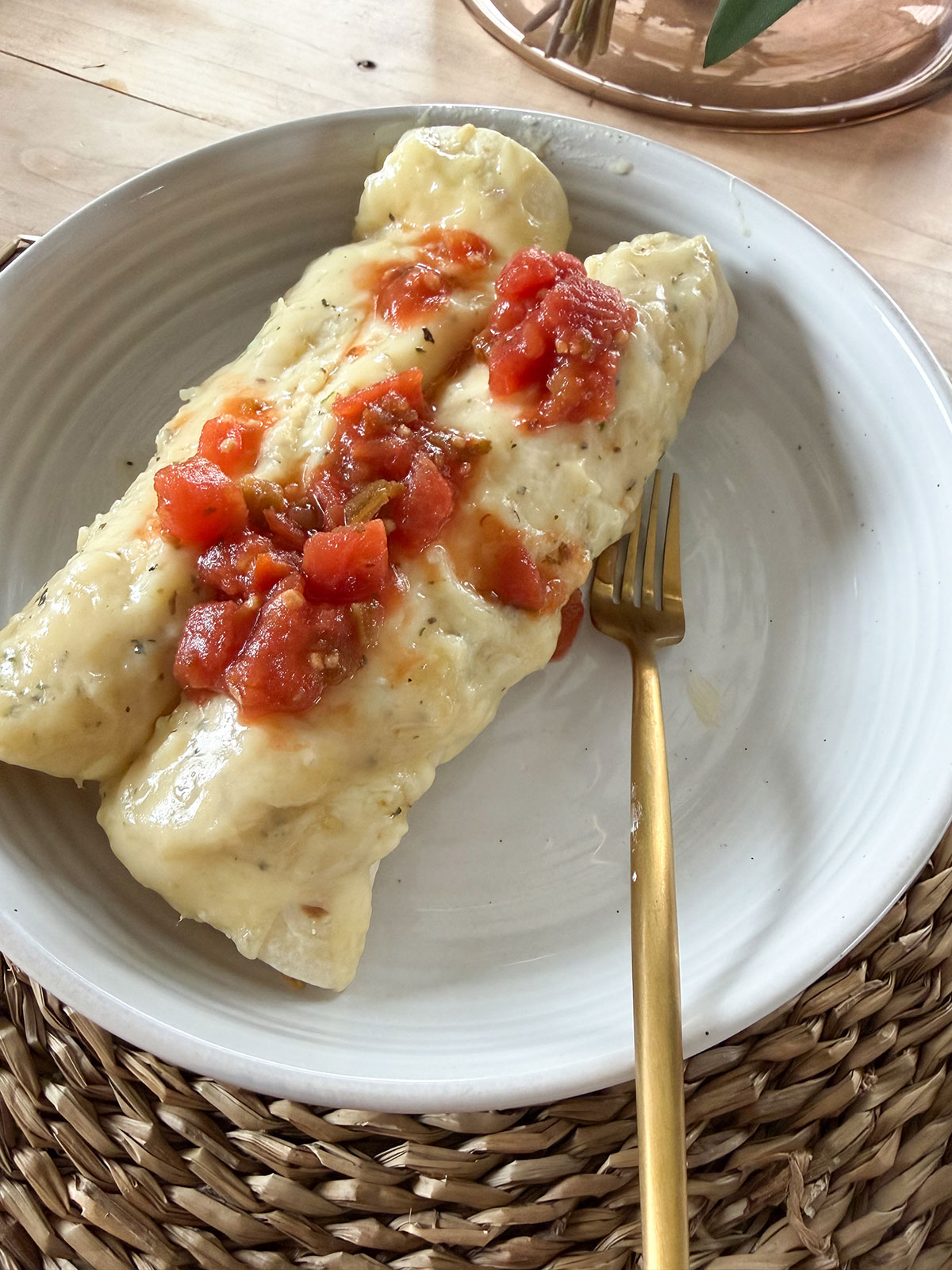 A white plate with white chicken enchiladas and a gold fork.