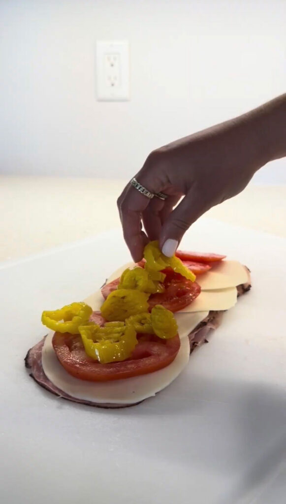 A hand layering ingredients on a sandwich for chopped Italian sliders.