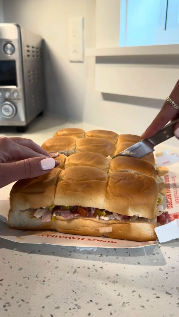 A hand slicing Italian sliders into individual sandwiches.