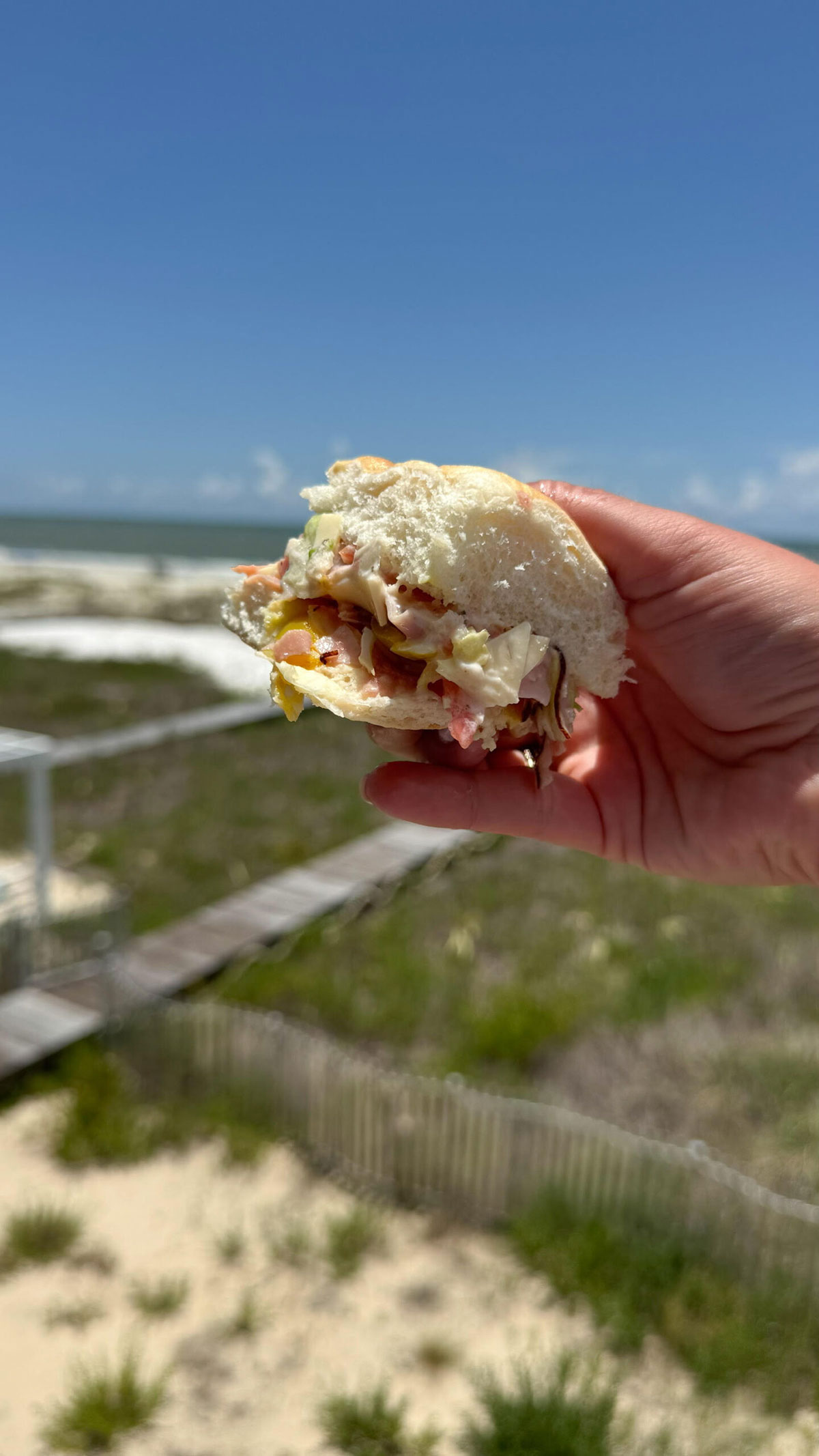 A hand holding up chopped Italian slider at the beach.