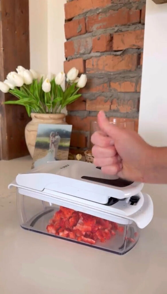 A hand using a chopper to chop strawberries.