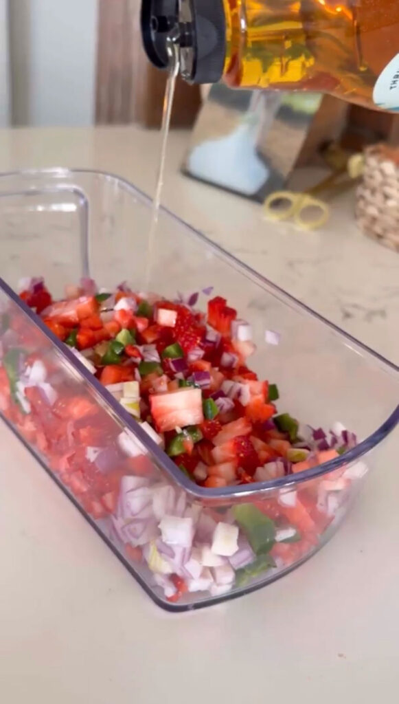 Strawberry salsa ingredients in a plastic container with agave being added.