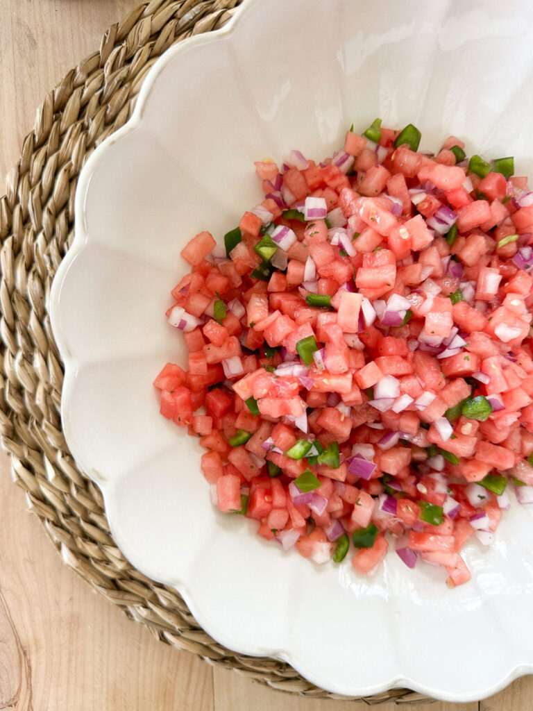 A white bowl with watermelon salsa on top of a wicker placemat.