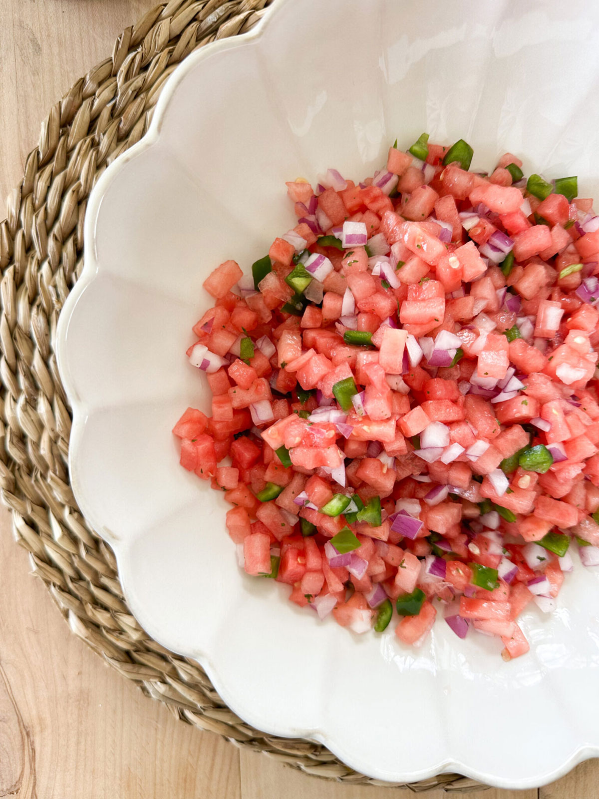 A white bowl with watermelon salsa on top of a wicker placemat.