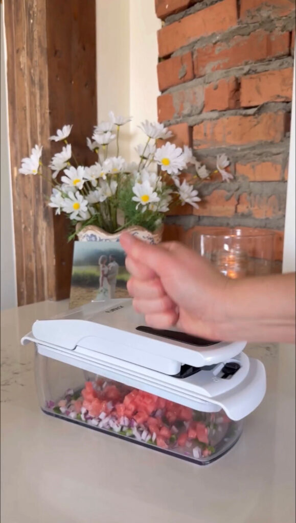 A hand using a chopper to cut ingredients for watermelon salsa.